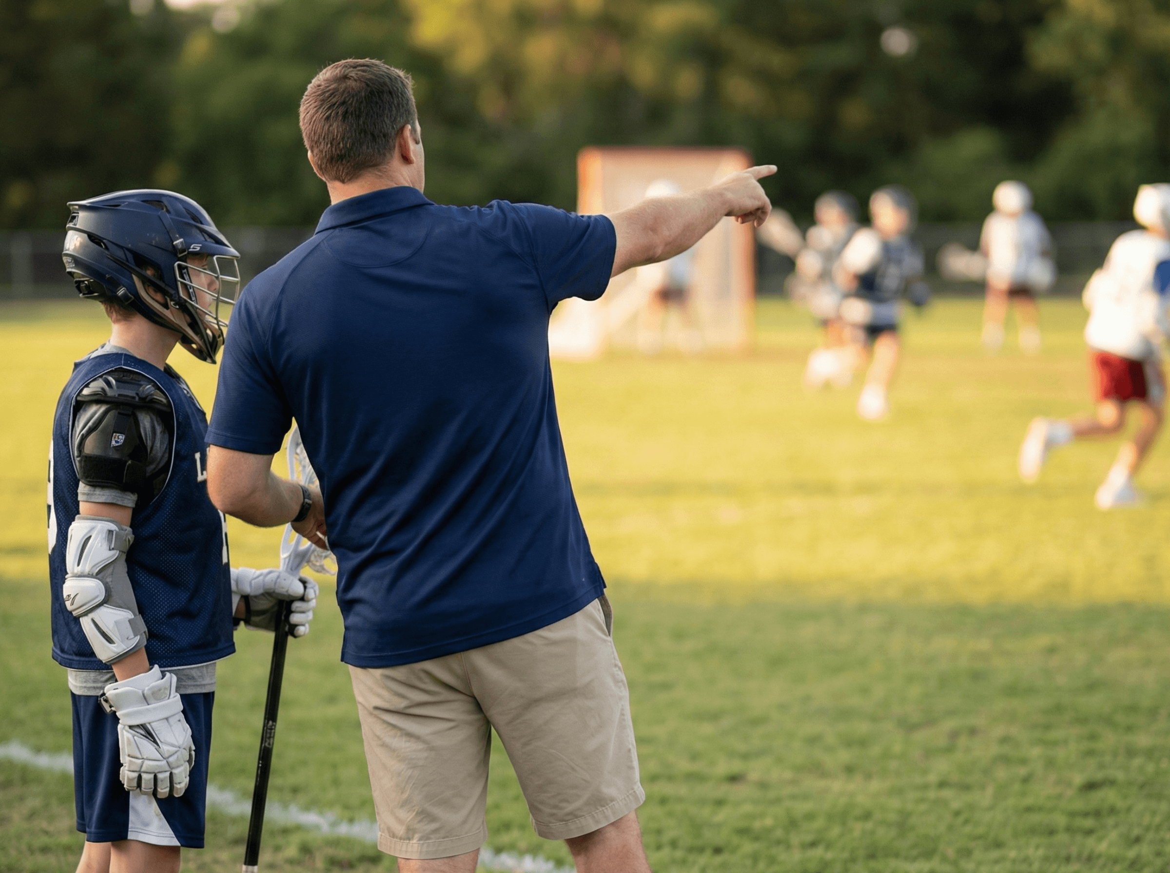 POWLAX play designer open on a tablet beside a phone showing a practice plan, on a turf lacrosse field with a goal behind