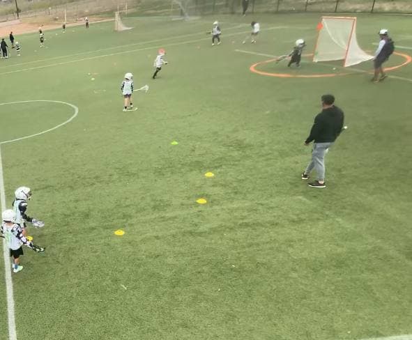 An overhead view of a practice field, two groups of youth players running drills at the same time, a coach standing between them.