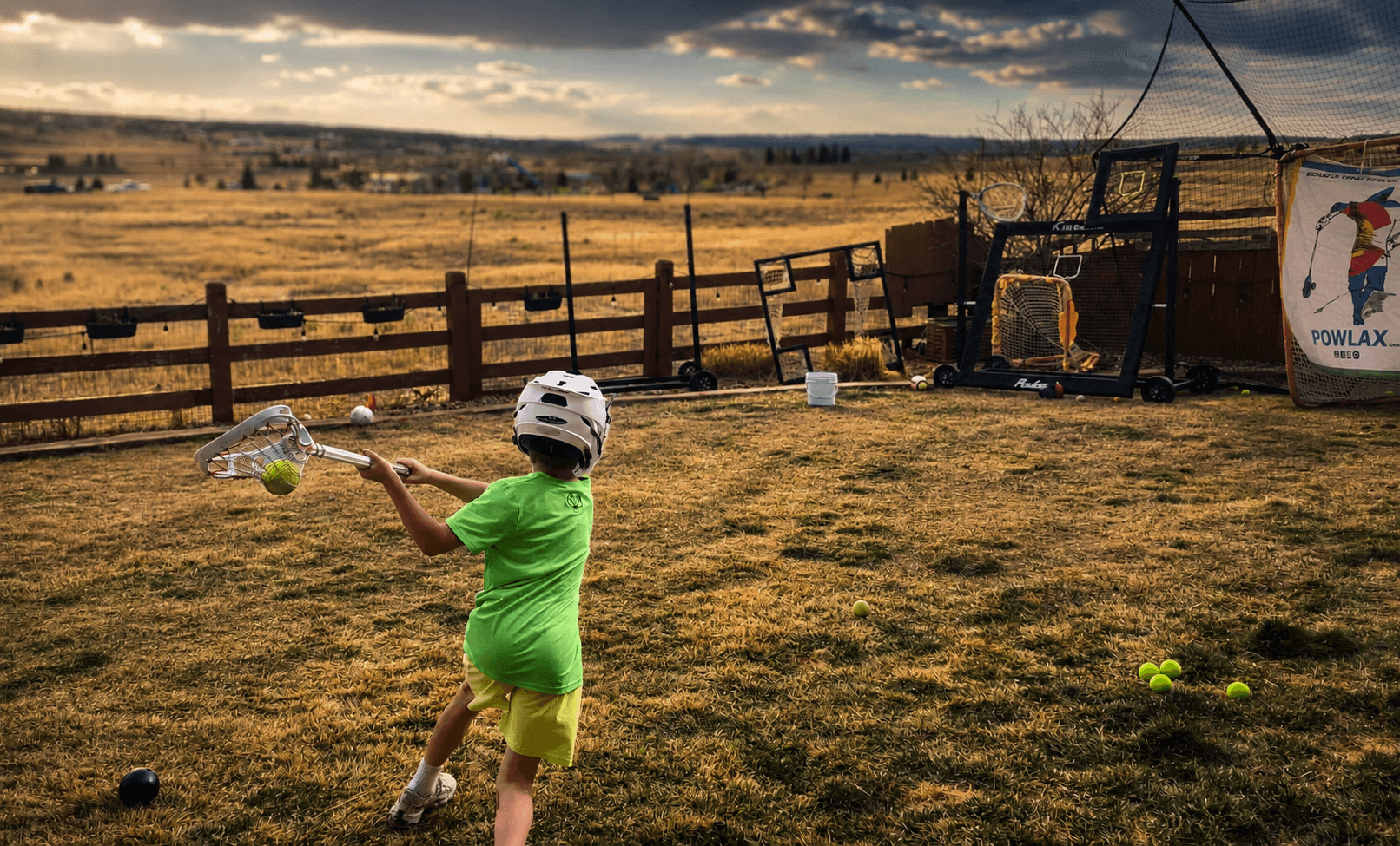 A young lacrosse player training in the backyard with a stick and a phone showing a workout